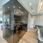 This transitional home wine cellar includes glass walls and door, and custom wooden racking.